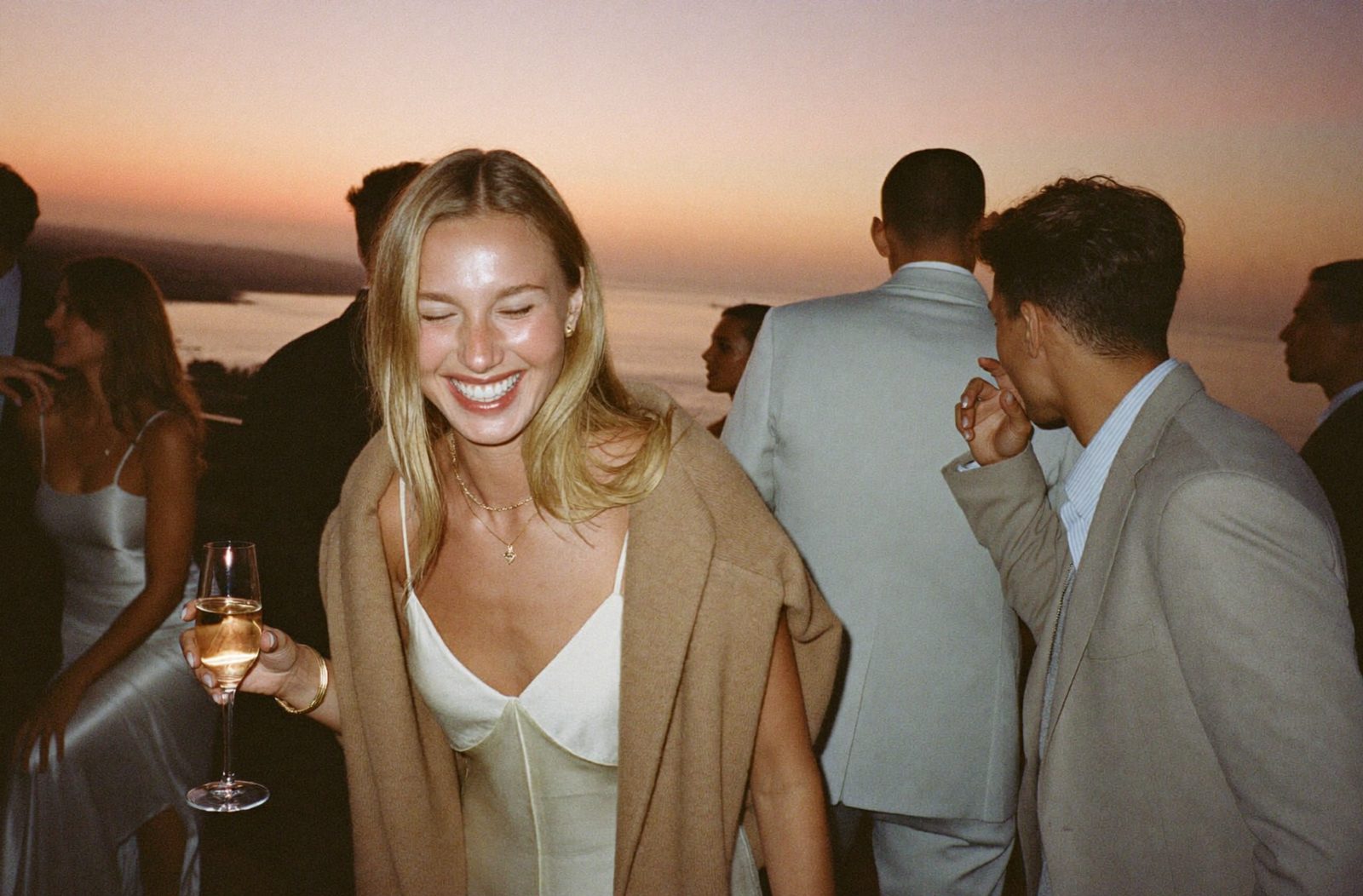 Blonde woman laughing with champagne at a rooftop party at sunset
