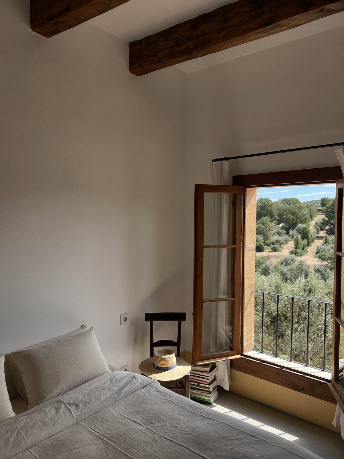 A whitewashed bedroom with chestnut beams and shutters open to the olive trees