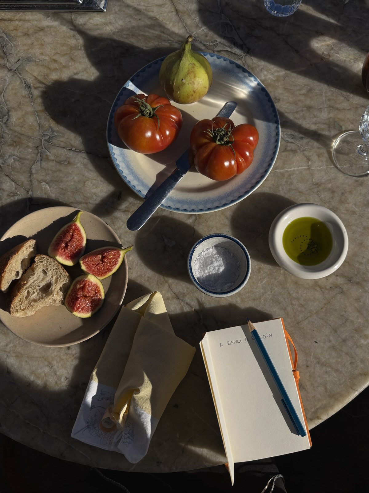 Tomatoes, figs, bread, olive oil and an open notebook on a marble table