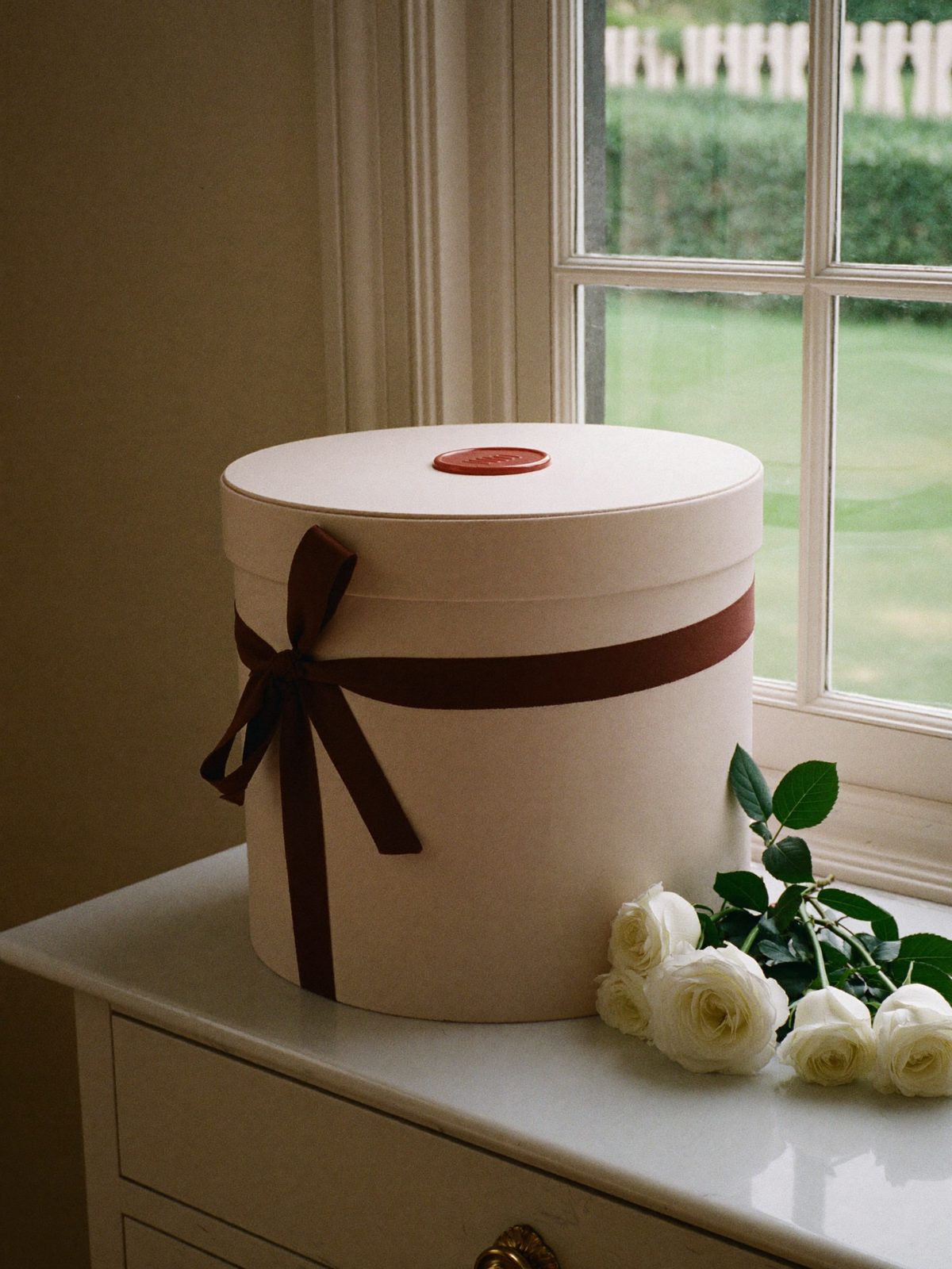 A pale blush hatbox style cake box tied with a cocoa silk ribbon and sealed in red wax on a marble console